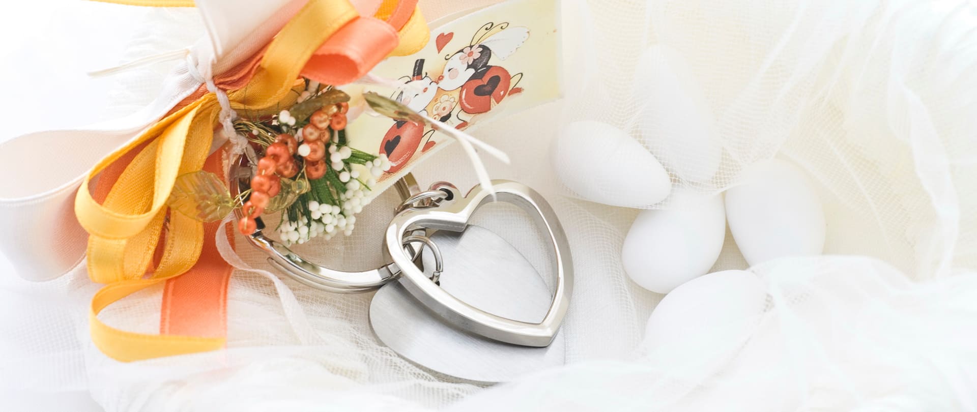 Cuori a fiori, bouquet e un ciondolo a forma di cuore argento su tulle bianco: un piccolo regalo romantico legato a tempo di nozze.