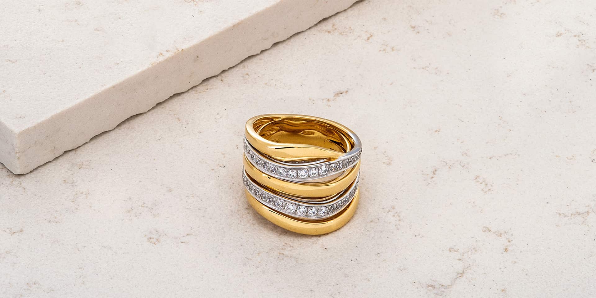 Anello in oro giallo con due righe di diamanti incastonati, posto su una superficie chiara.
