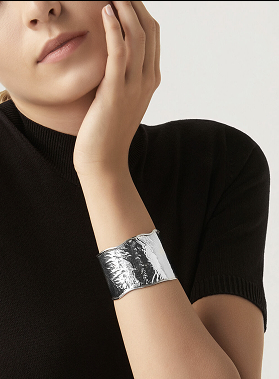 Braccia incrociate, polso avvolto da nastro argentato metallico, look minimal con maglia nera.