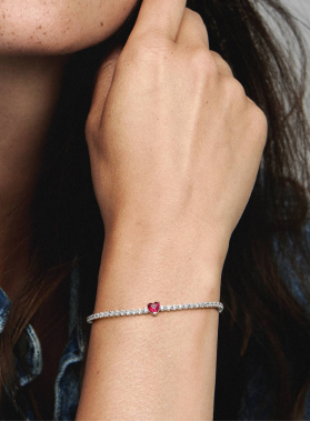 Braccia femminili con braccialetto elegante: perle chiare e pietra centrale rossa su sfondo sfumato.