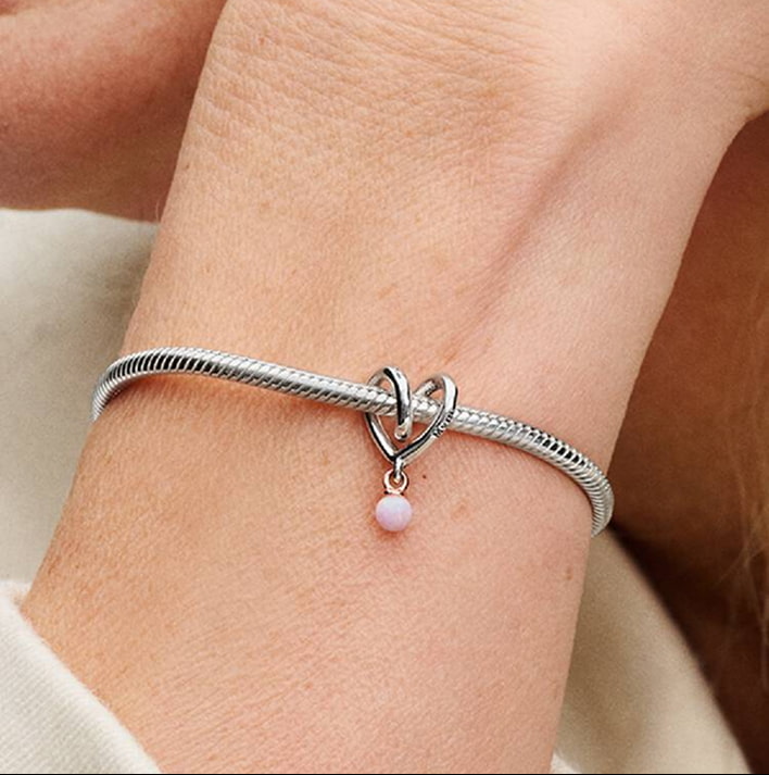 Braccialetto argento con ciondolo a cuore intrecciato e ciondino a perla lilla, indossato sul polso.