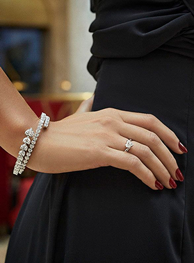 Mano femminile con anello scintillante e bracciale rosa, una cornice elegante su abito nero in primo piano.