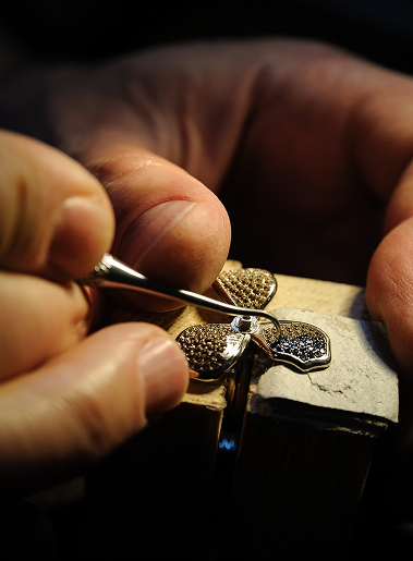 Praticante lavora su un anello con pietra, strumenti da orefice e pinza, messa a lavorare su una base metallica.