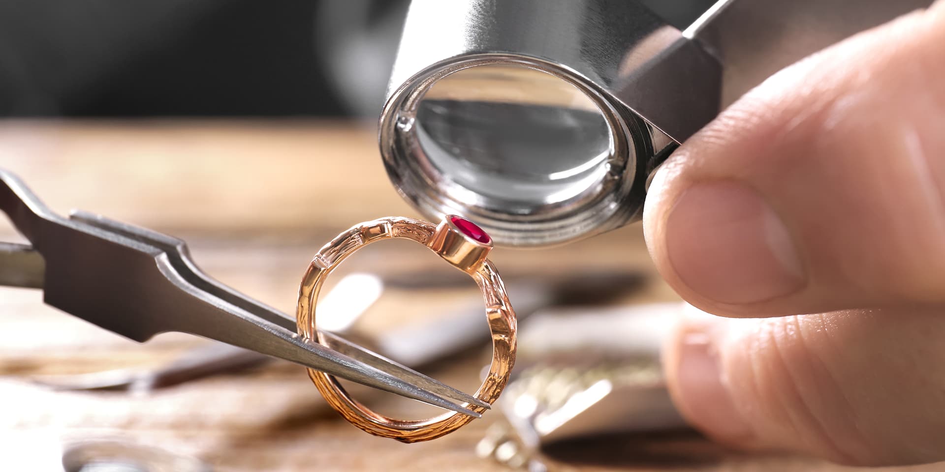 Anello d'oro con brillante rubino, posato per ispezione con lente d'ingrandimento e pinza su tavolo da gioielleria.