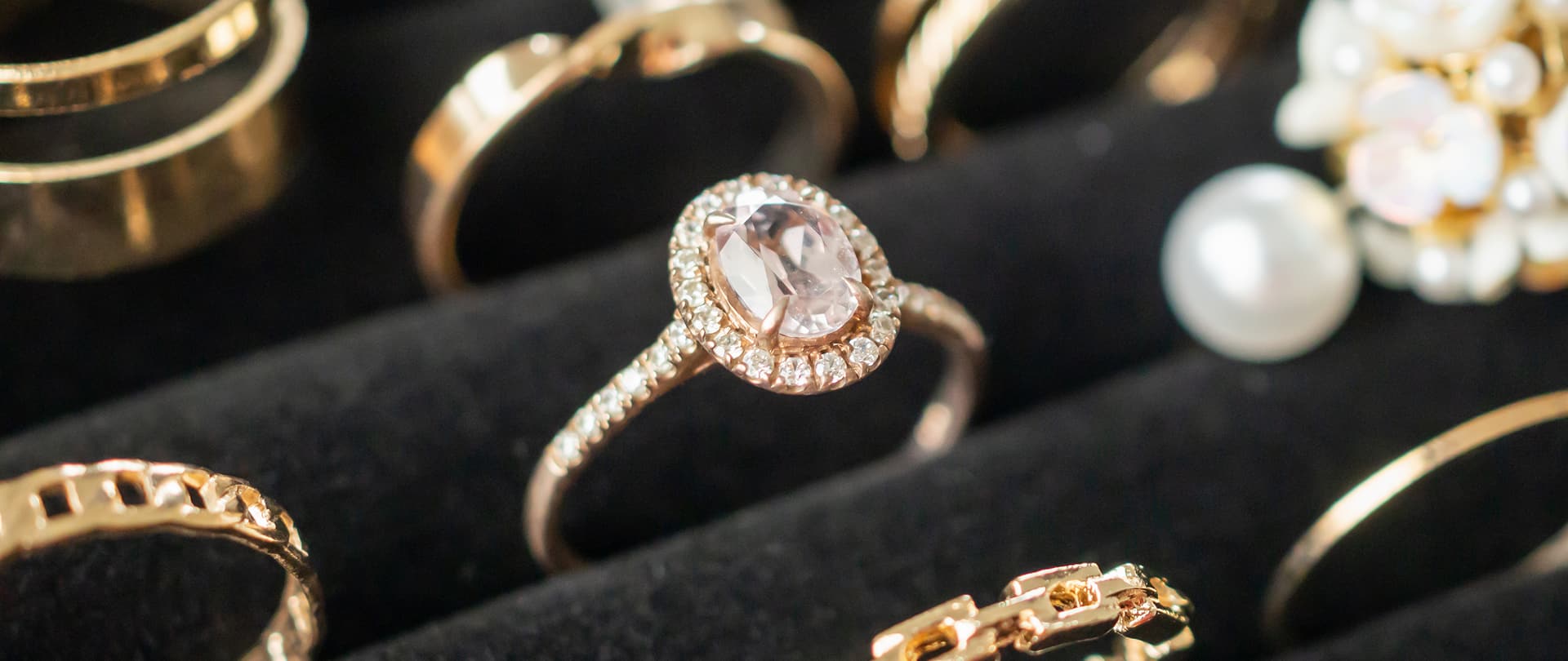 Anello con pietra centrale ovale rosa chiaro circondata da microcarati, gioielli lucidi su fondo scuro.