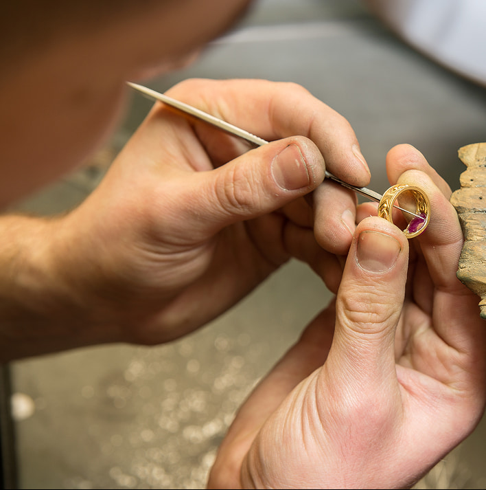 artigiano al lavoro su un anello con pietra rosa, attrezzi e una pietra da un lato, mani ferme e precisione durante la lavorazione