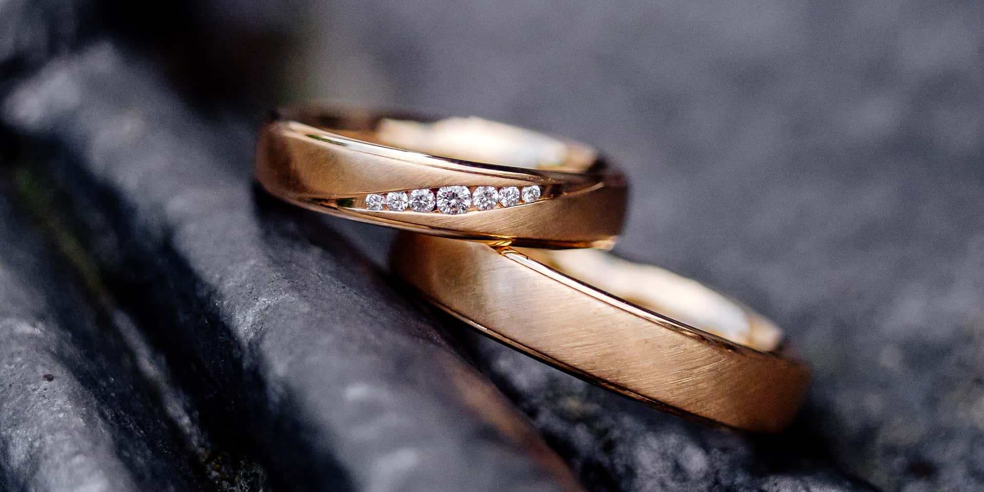 Due anelli intrecciati in oro rosa con paino di piccoli diamanti incastonati, su sfondo scuro e sfumato.