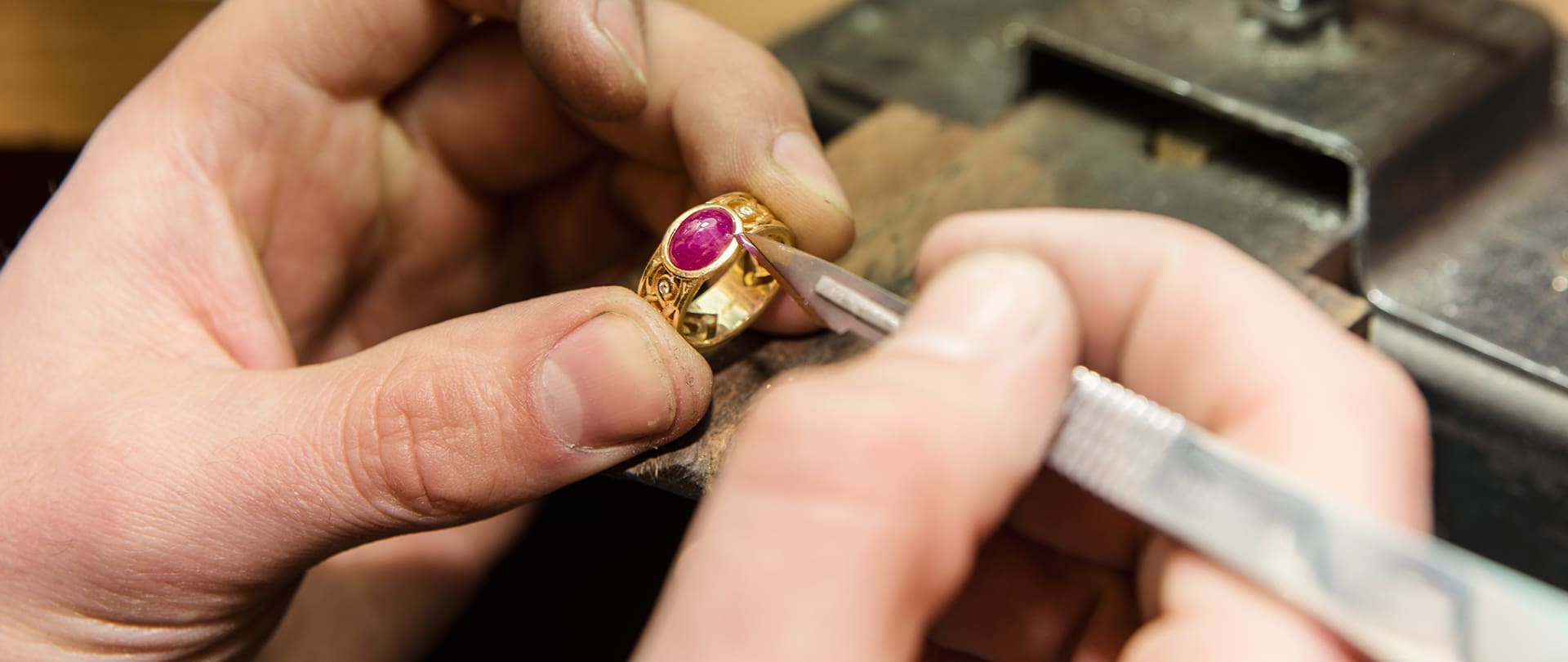Lavorazione artigianale di un anello dorato con pietra rossa, mani che lucidano e rifinire dettagli con strumenti da gioielleria.