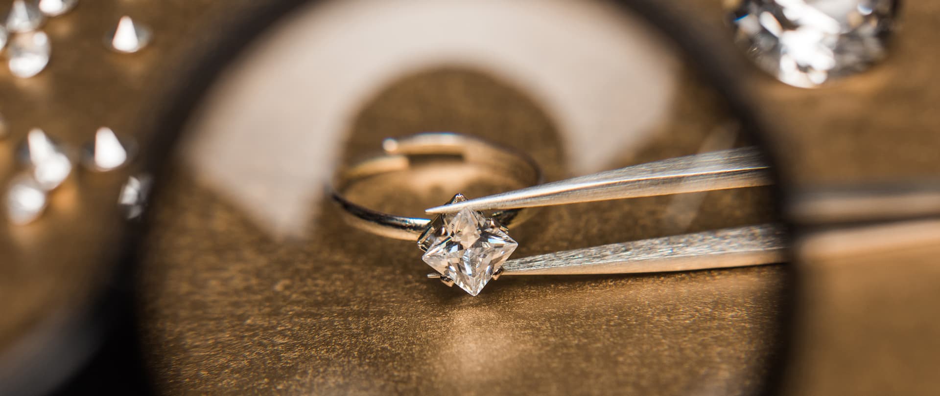 Anello nuziale con pietra incastonata, posato su superfice dorata, con attrezzi da gioielleria in primo piano.