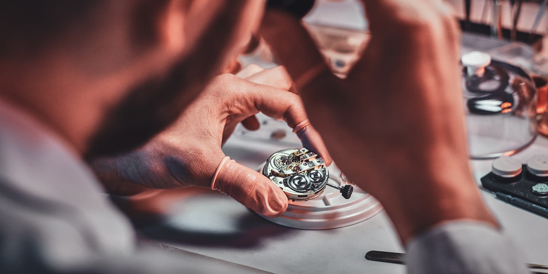 artigiano in laboratorio che sistema un orologio meccanico, movimenti e strumenti intorno su una superficie di lavoro